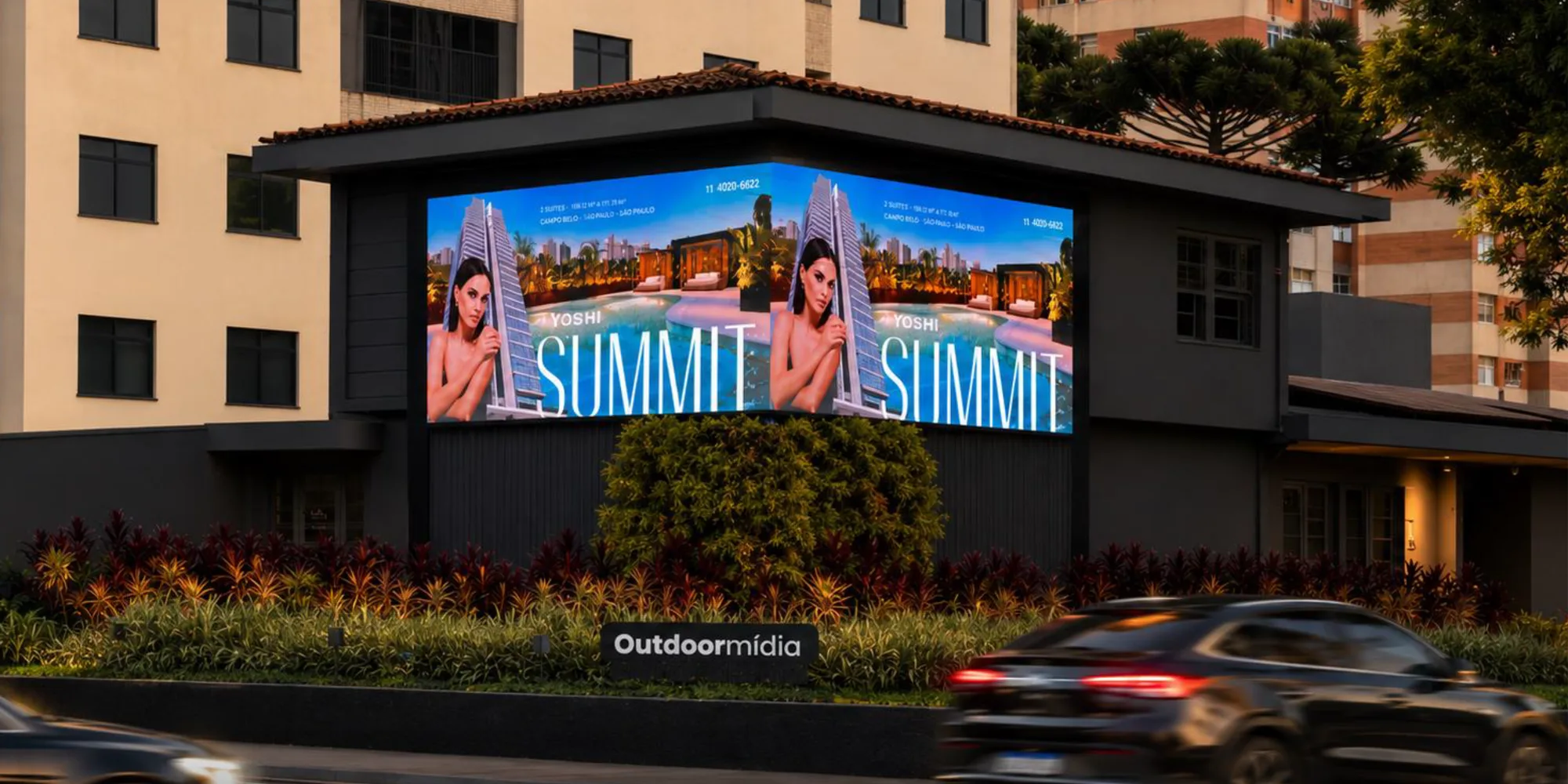 Esquina digital com duas faces de LED em ângulo exibindo uma campanha, sobre edifício em avenida