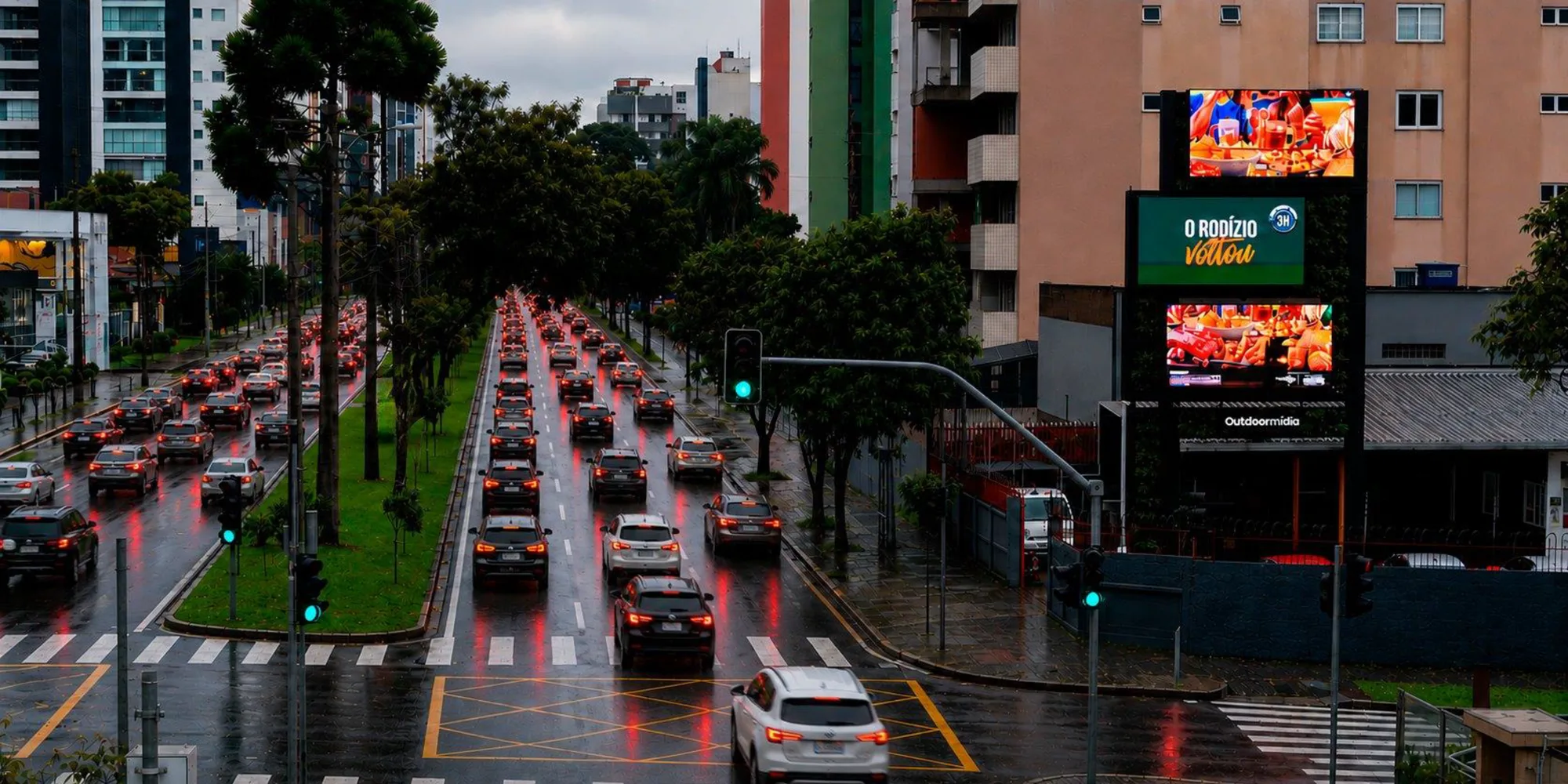 Painéis digitais verticais na avenida ao anoitecer, com trânsito intenso e pista molhada