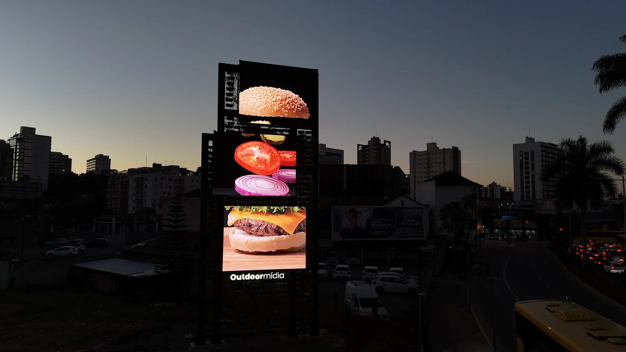 Três painéis digitais verticais em composição de cascata ao entardecer, com o skyline da cidade ao fundo