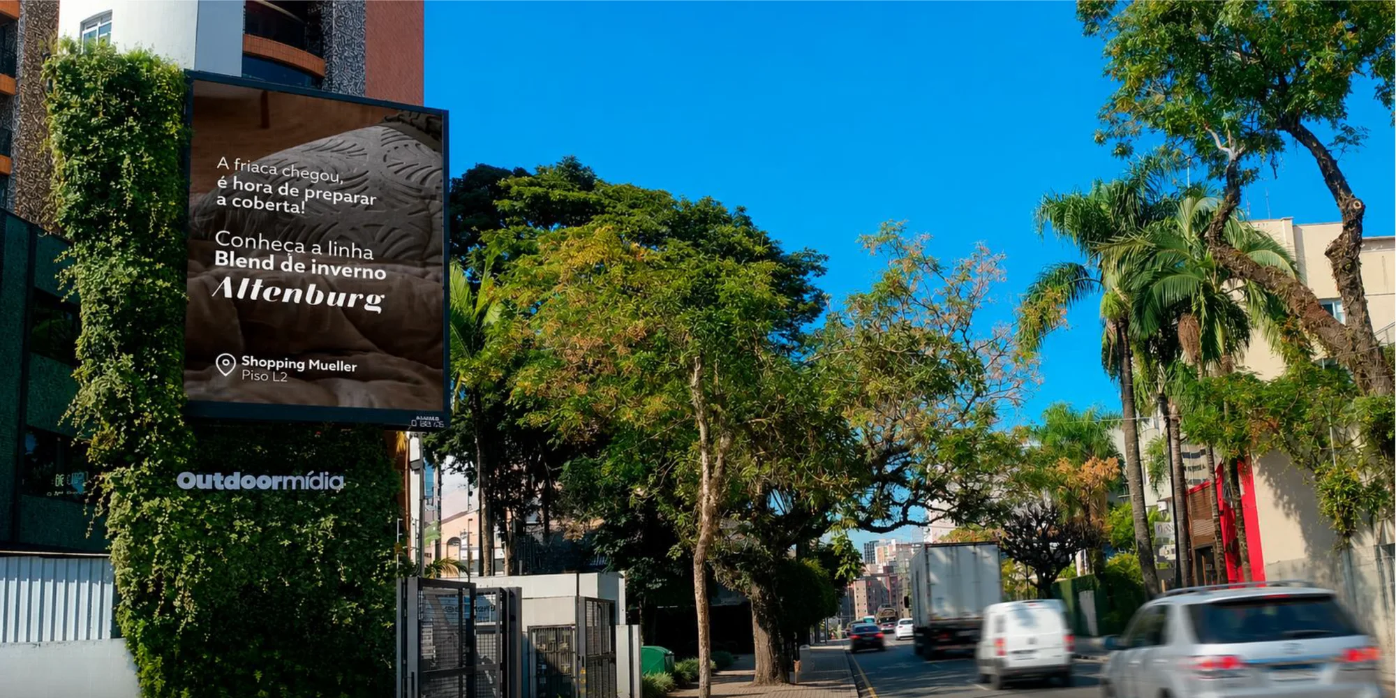 Painel publicitário emoldurado por vegetação viva em avenida arborizada