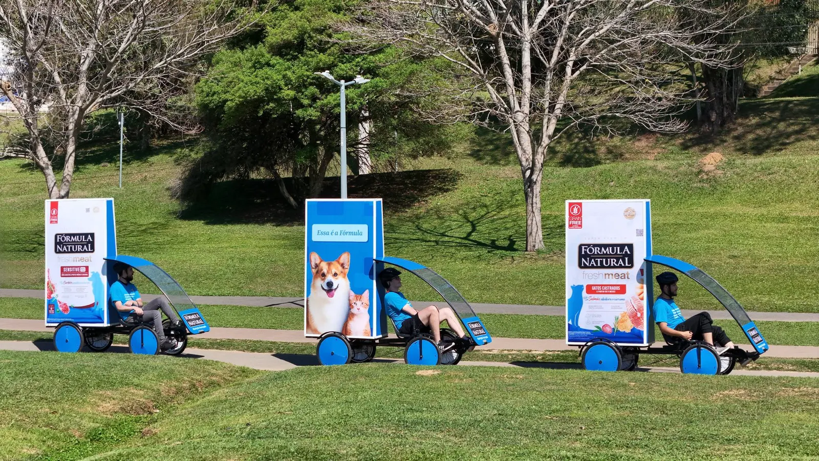 Trio de Bike Mídia da Outdoormídia com a campanha da Fórmula Natural, circulando pela ciclovia de um parque de Curitiba