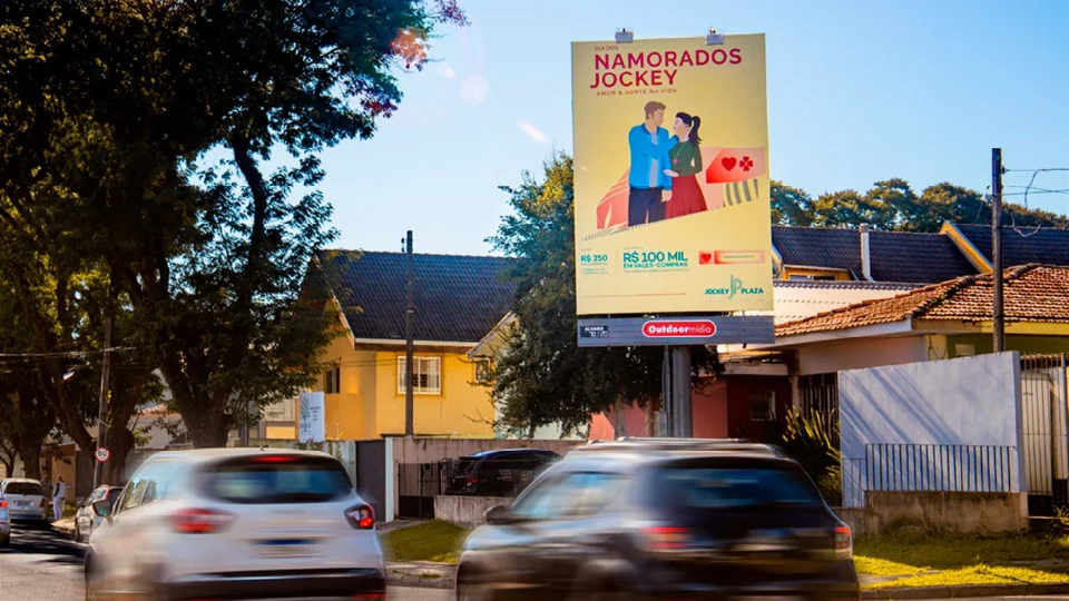 Painel Top Sight estático da Outdoormídia com campanha de Dia dos Namorados do Jockey Plaza, sobre avenida com carros passando