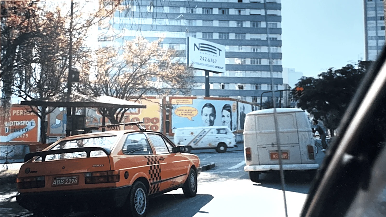 Foto de arquivo de uma avenida de Curitiba com outdoors ao fundo, um táxi laranja e uma Kombi em primeiro plano
