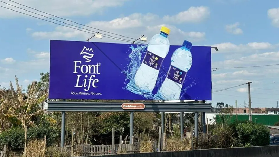 Painel 9×3 com campanha da Font Life à beira da estrada, com a marca Outdoormídia na base da estrutura