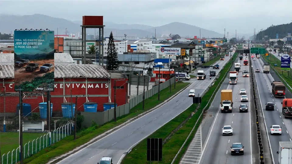 Painel Super Top 8×12 com campanha da Jeep à margem de rodovia de pista dupla, com o fluxo de caminhões e carros ao lado