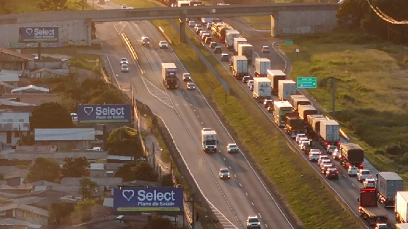 Três billboards Rodovias em sequência à beira da rodovia, com a campanha da Select Plano de Saúde, vistos do alto ao entardecer